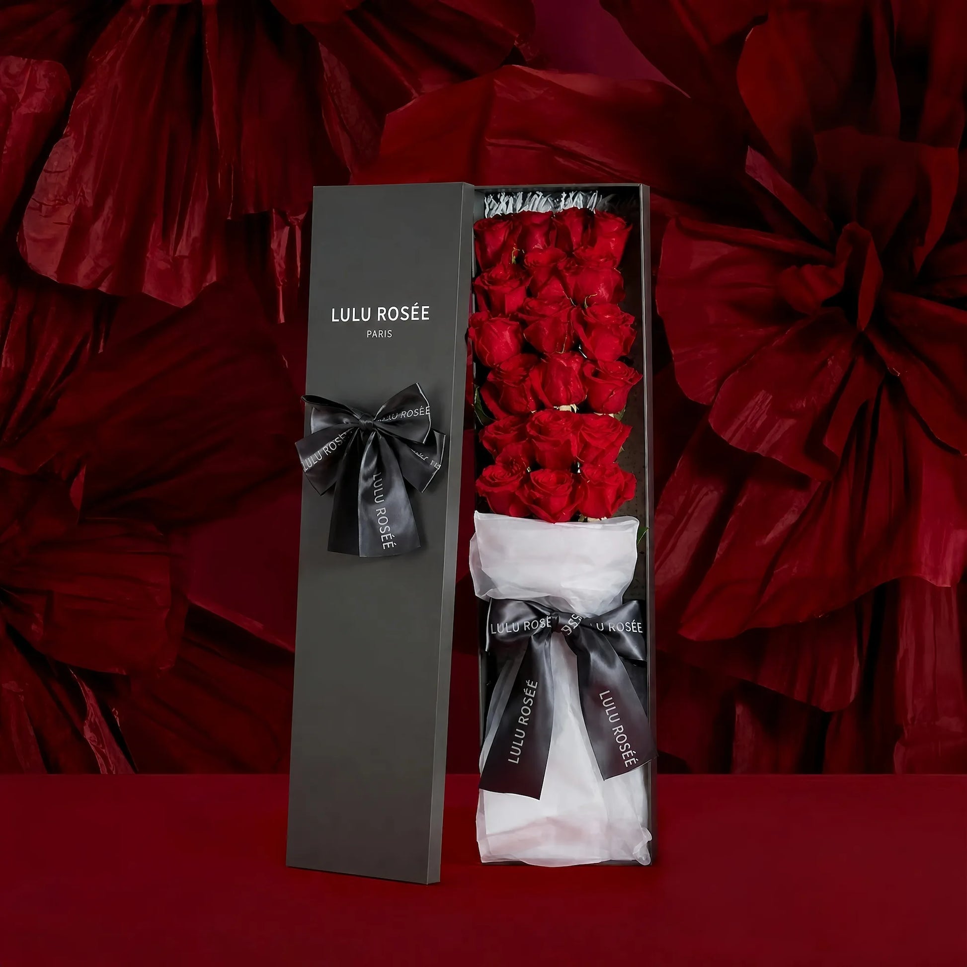 LULU ROSÉE Grande Long Stem Preserved Rose Box, luxury long rectangular gift box filled with long stem red preserved roses, red rose petal backdrop aesthetic shot, decorated with elegant grey satin ribbon, customizable flower colors, everlasting romantic floral souvenir for Valentine’s Day, anniversary & birthday gifting