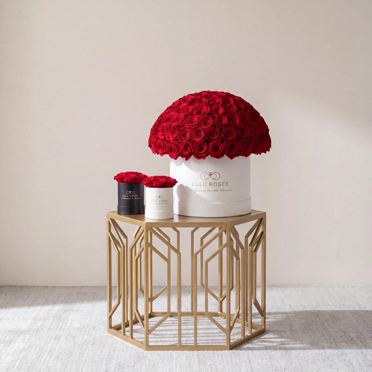 Three flower boxes with red roses on a gold side table against a beige wall.