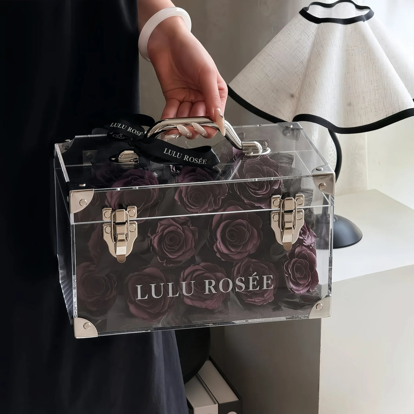 LULU ROSÉE Petite Eternal Acrylic Handbag Rose Box, small transparent acrylic handbag-shaped gift box filled with dark purple preserved roses paired with black ribbon minimalist indoor shot, customizable flower color options, mini luxury everlasting floral souvenir for birthday, anniversary & romantic gift giving